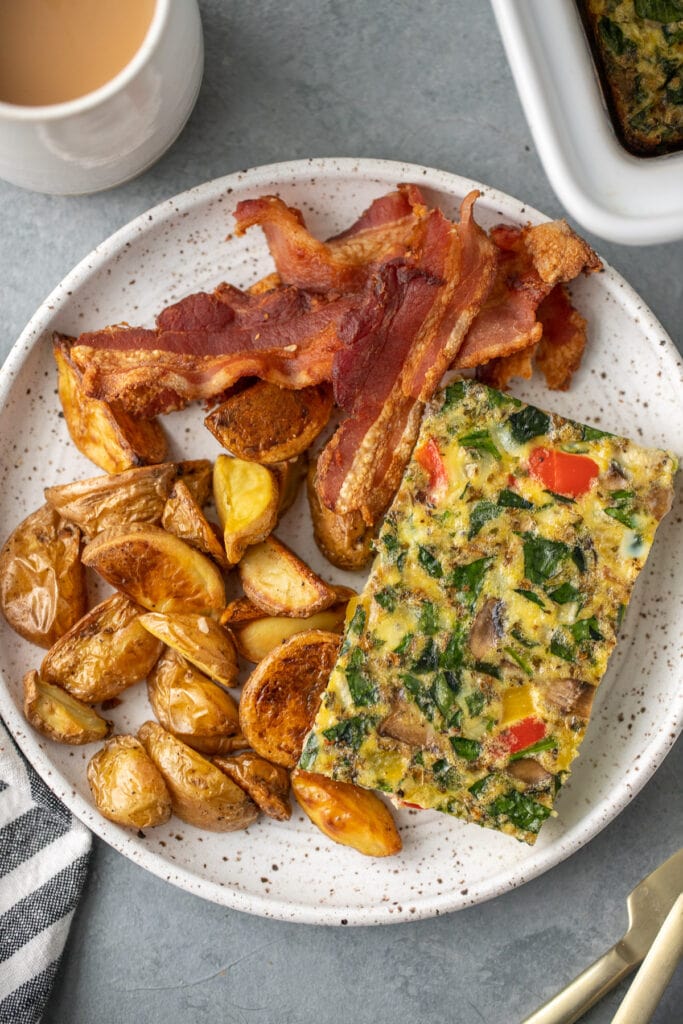 an overhead shot of healthy egg bake on a white plate with bacon and crispy potatoes