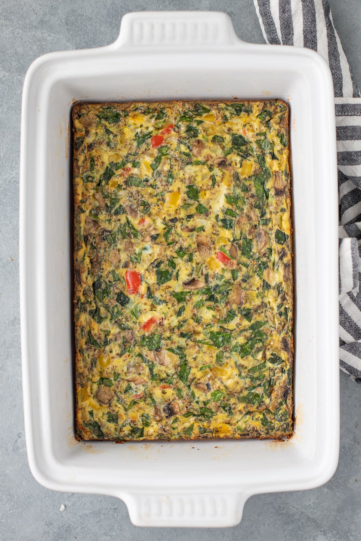 an overhead shot of an egg bake in a white casserole dish on a grey background
