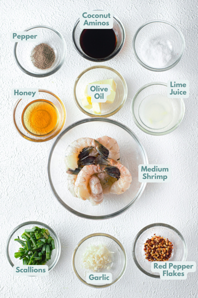 Ingredients for honey garlic shrimp in clear bowls: medium shrimp, butter or olive oil, minced garlic, honey, coconut aminos, fresh lime juice, black pepper, red chili flakes, chopped scallions