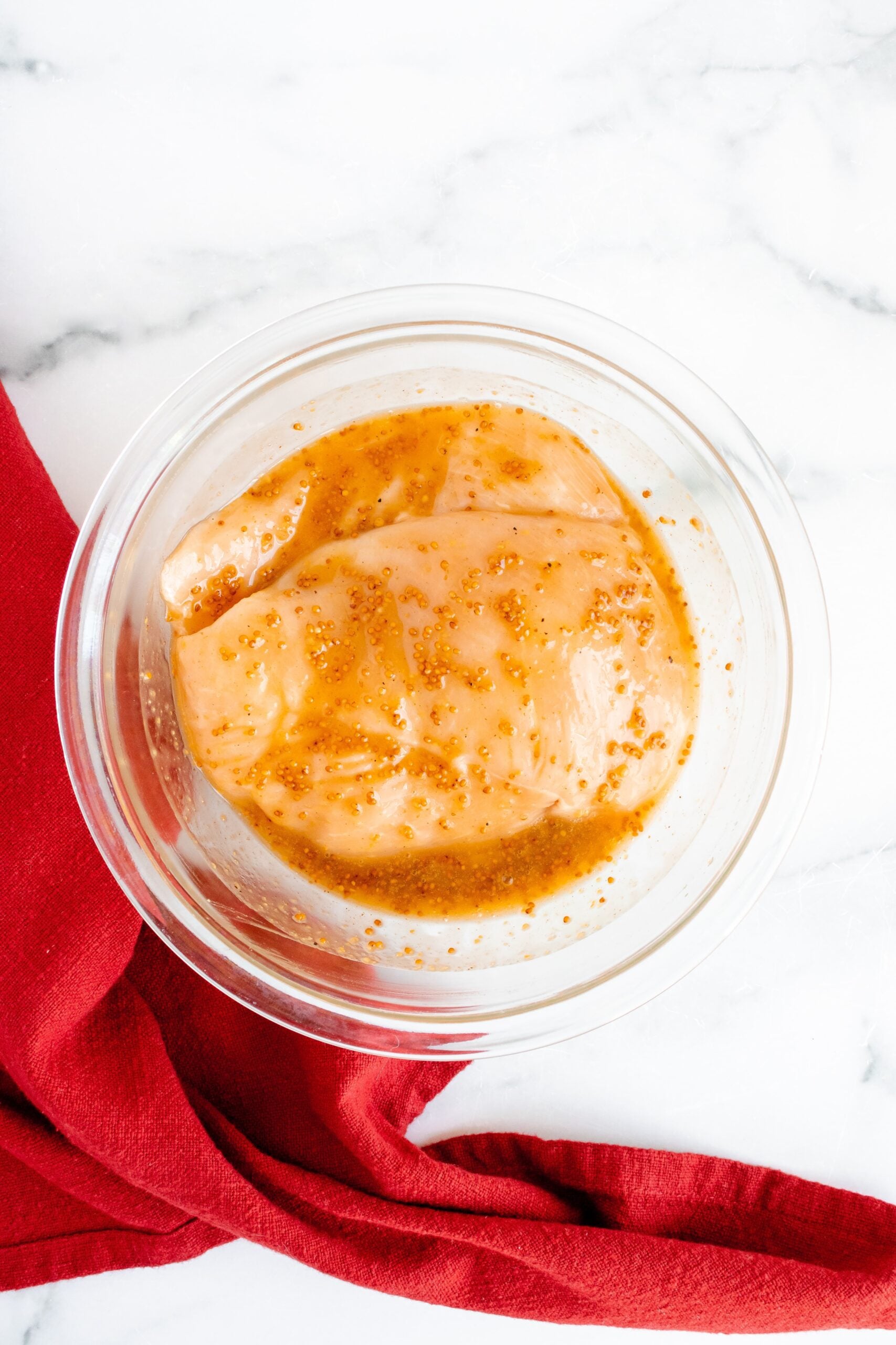Chicken breast marinating in a honey mustard dressing in a clear bowl for a salad