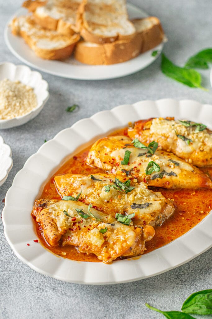 Instant pot chicken parmesan on a white platter with a plate of toast and parmesan cheese in the background