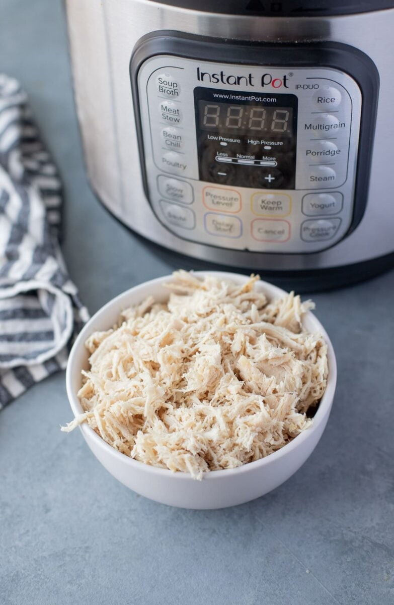 Easy Instant Pot Shredded Chicken in a blue bowl with a pressure cooker behind it