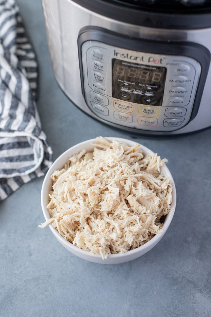 A bowl of instant pot shredded chicken with the pressure cooker in the background.
