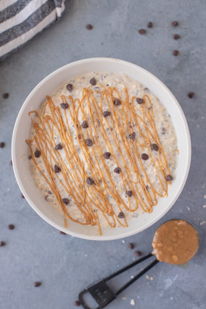 peanut butter overnight oats with chocolate chips and peanut butter drizzle on top with a tablespoon of peanut butter on the side