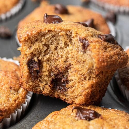 a banana protein muffin with a bite taken out of it sitting on a pan of muffins