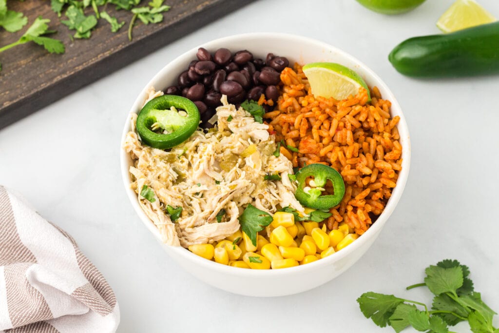 Salsa chicken verde in a white bowl with cooked black beans, corn, and Mexican rice.