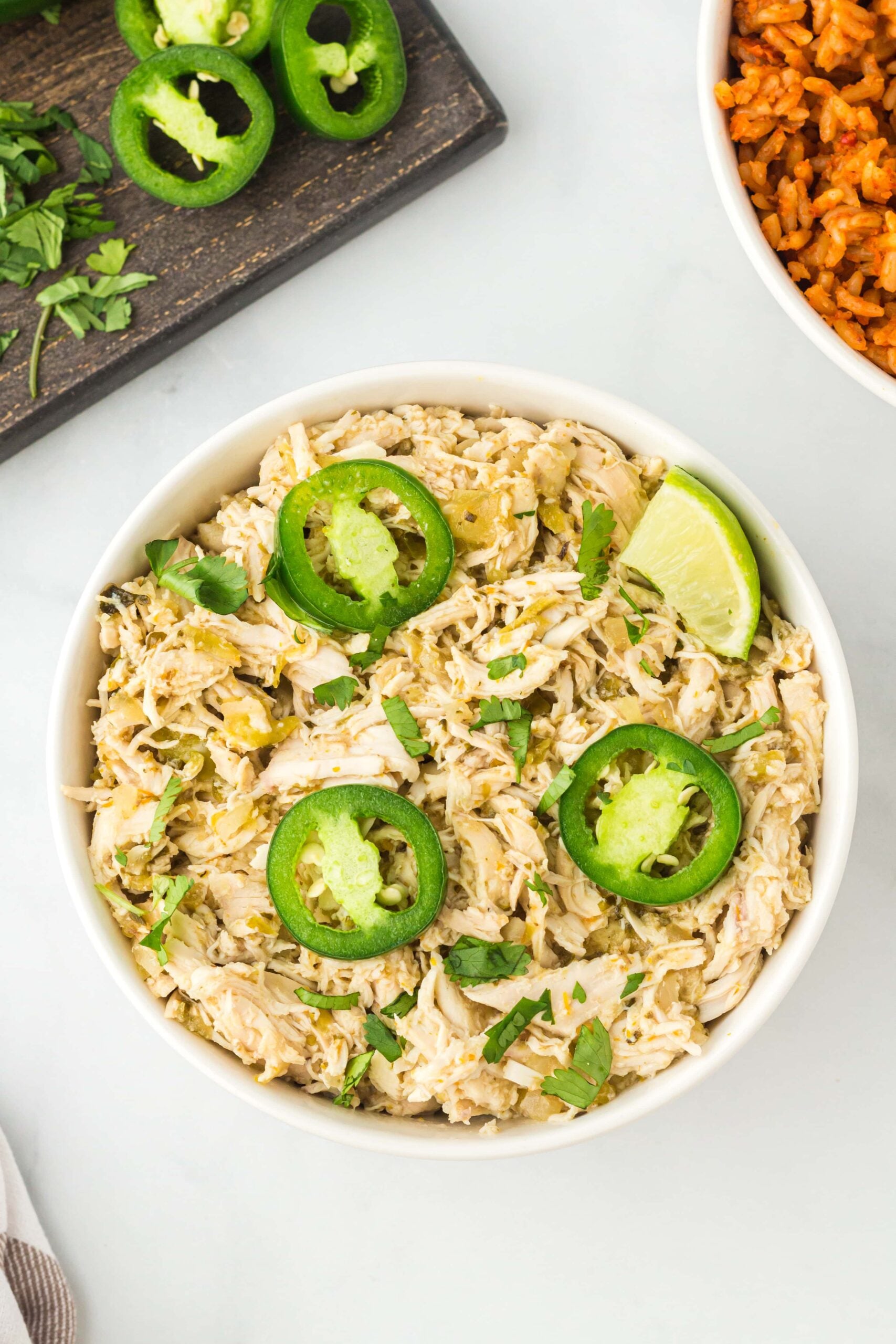 A white bowl of salsa verde chicken with jalapeño slices and a lime slice on top.