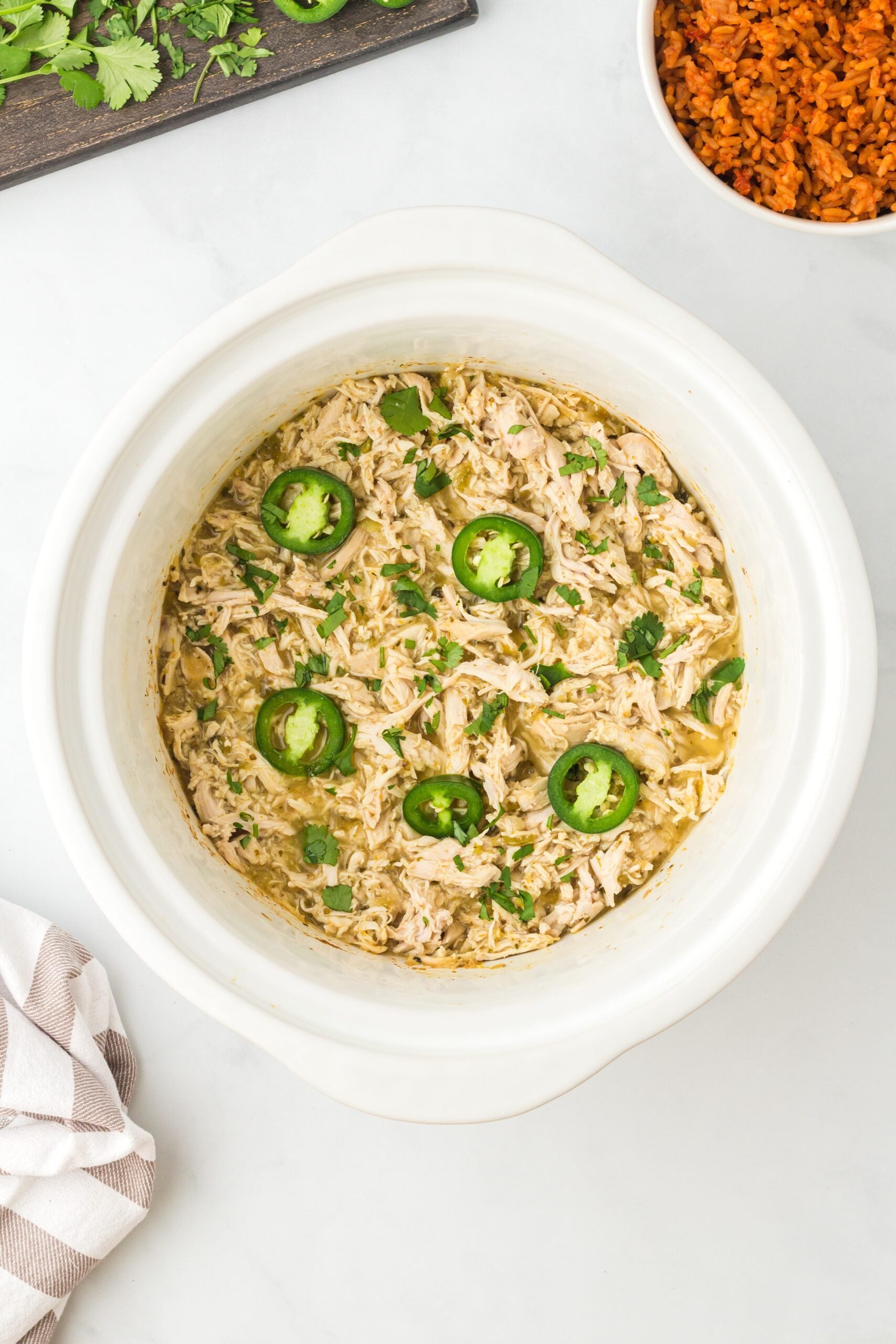 Overhead view of shredded white meat in a crock pot topped with fresh cilantro and jalapeno slices.
