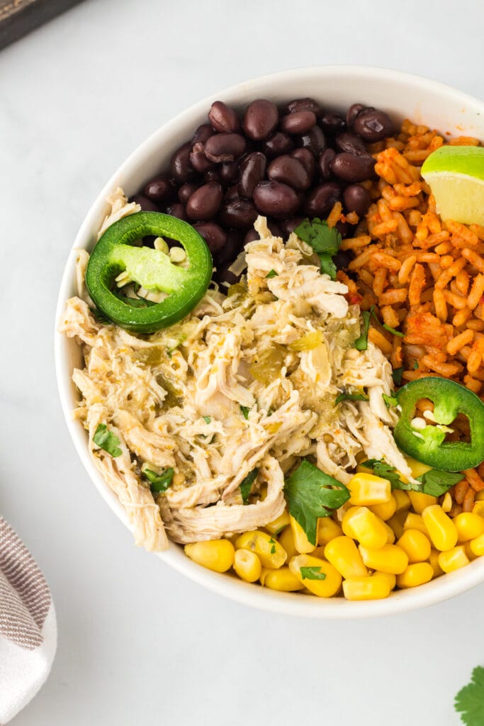 Overhead view of chicken verde in a bowl with black beans, Mexican rice, and corn niblets.