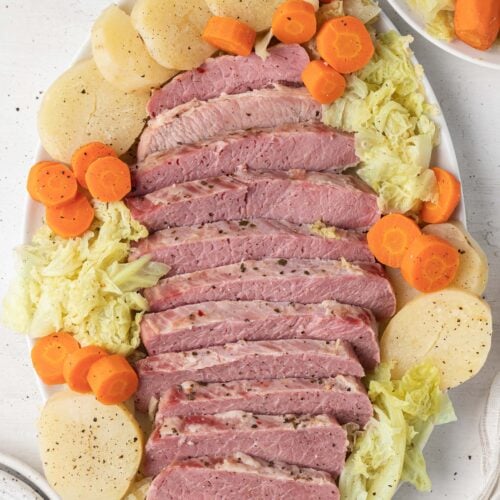 slow cooker corned beef on a white platter surrounded by cabbage, carrots and potatoes