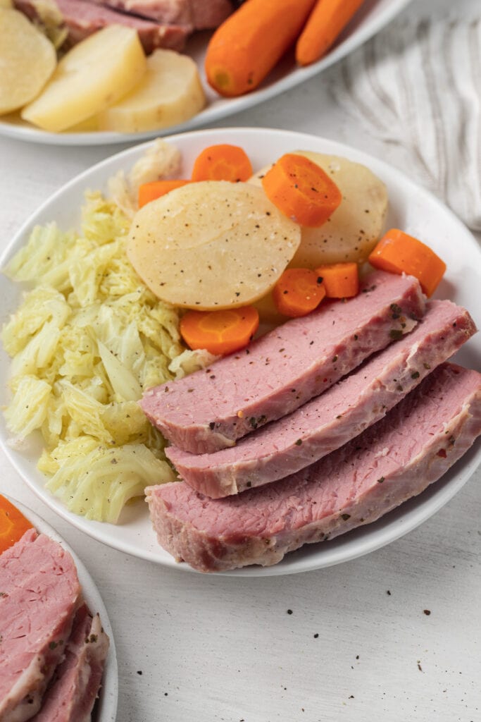 a white plate of slow cooker corned beef with cabbage, carrots and potatoes
