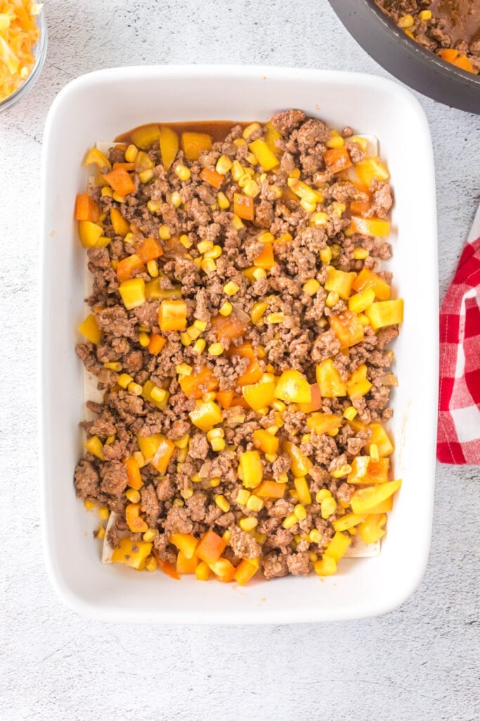 An overhead shot of an unbaked ground beef casserole in a white baking dish.