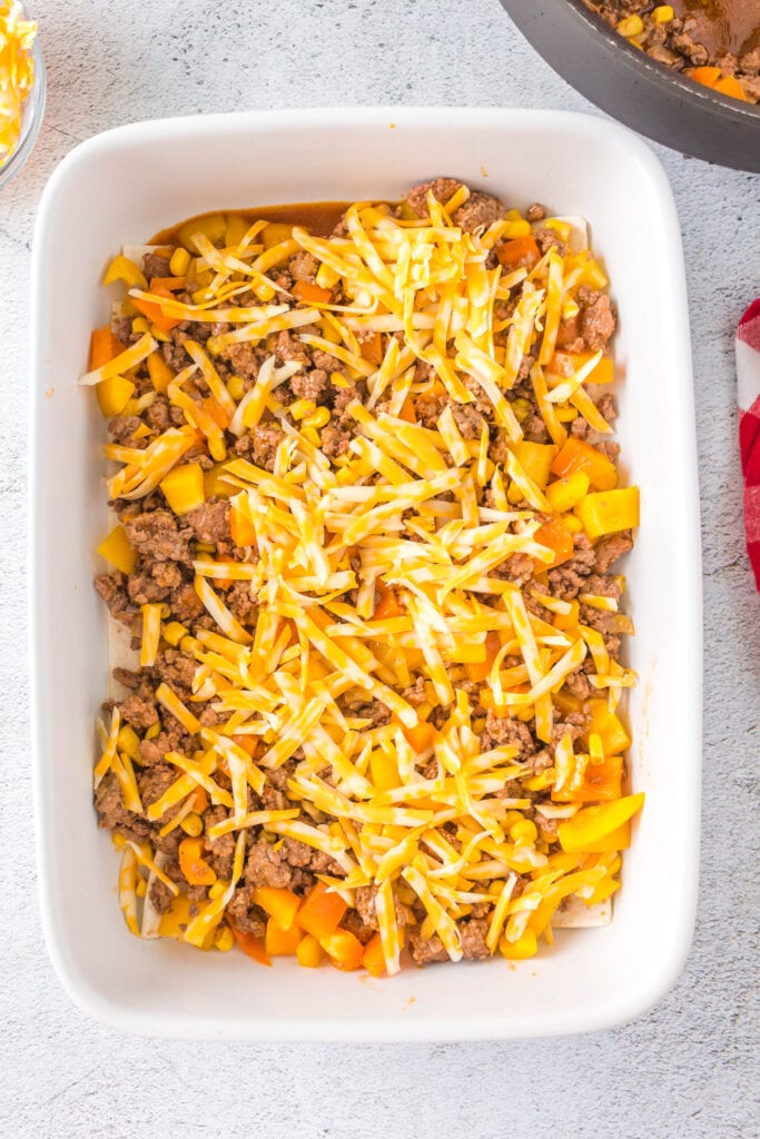 Overhead shot of shredded Mexican cheese layered over cooked beef and vegetables in a baking dish.