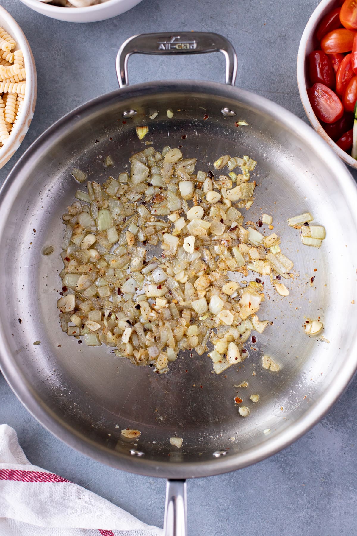 Sautéed onions, garlic, and spices in a pan for vegetable pasta on a grey background