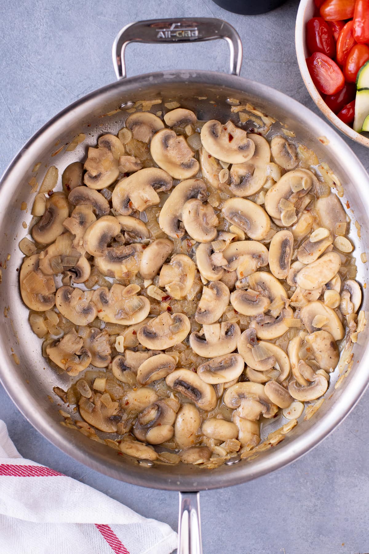 Sautéed onions, garlic, spices, mushrooms and white wine in a pan for pasta primavera on a grey background