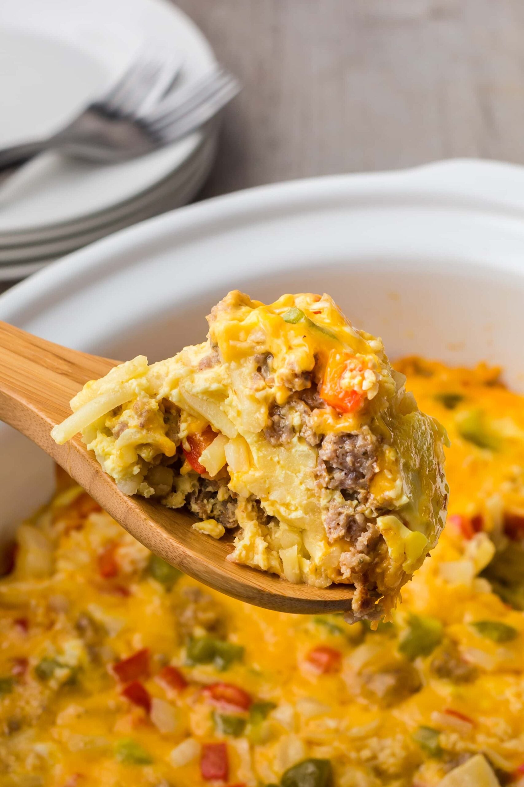 a wooden spoon of crock pot breakfast casserole with the crock pot full of casserole in the background