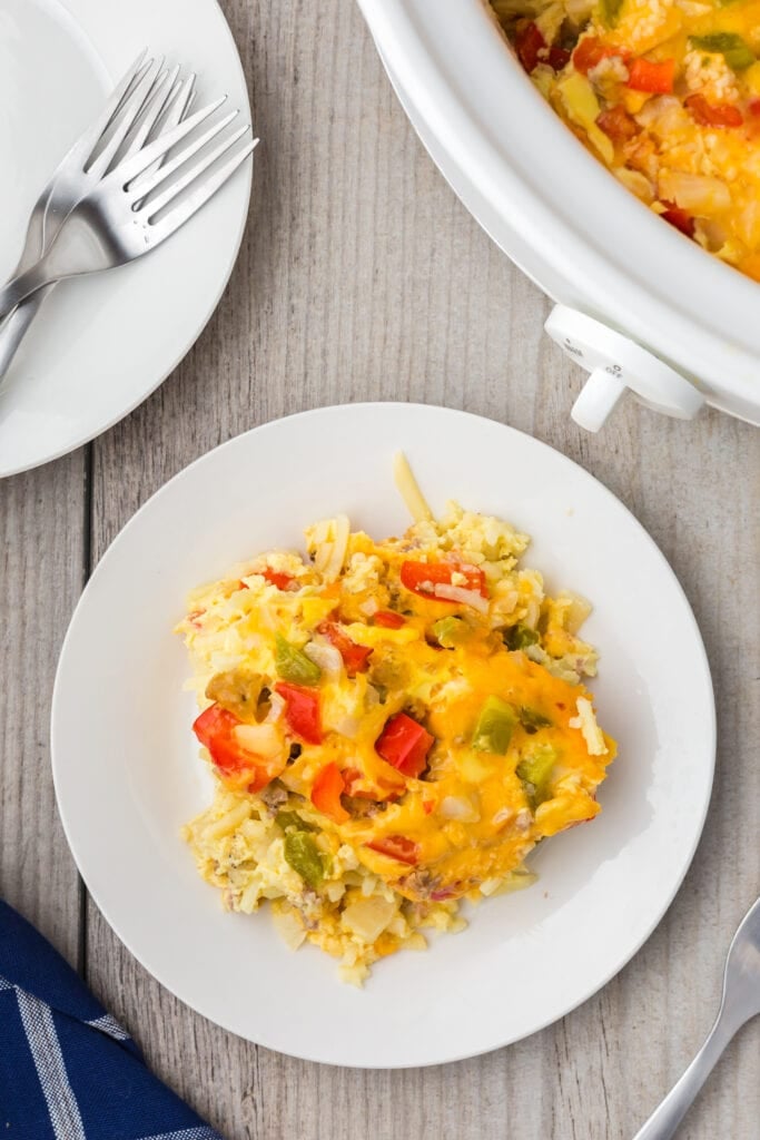 A white plate of crock pot breakfast casserole with the crockpot on the side