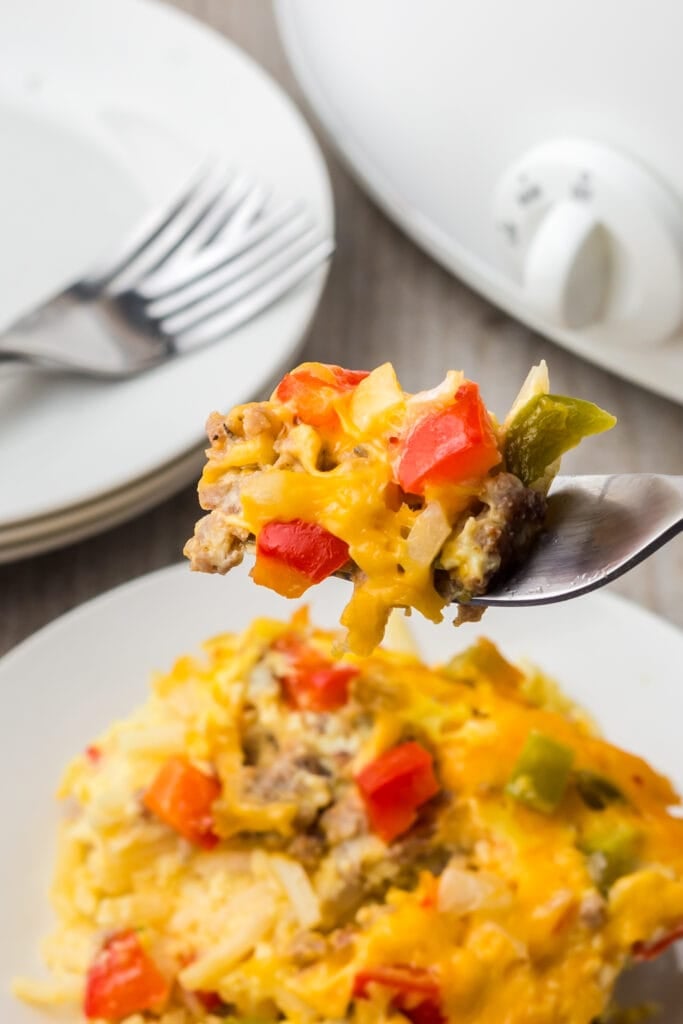 a fork taking a bite of crock pot breakfast casserole off a white plate of the casserole