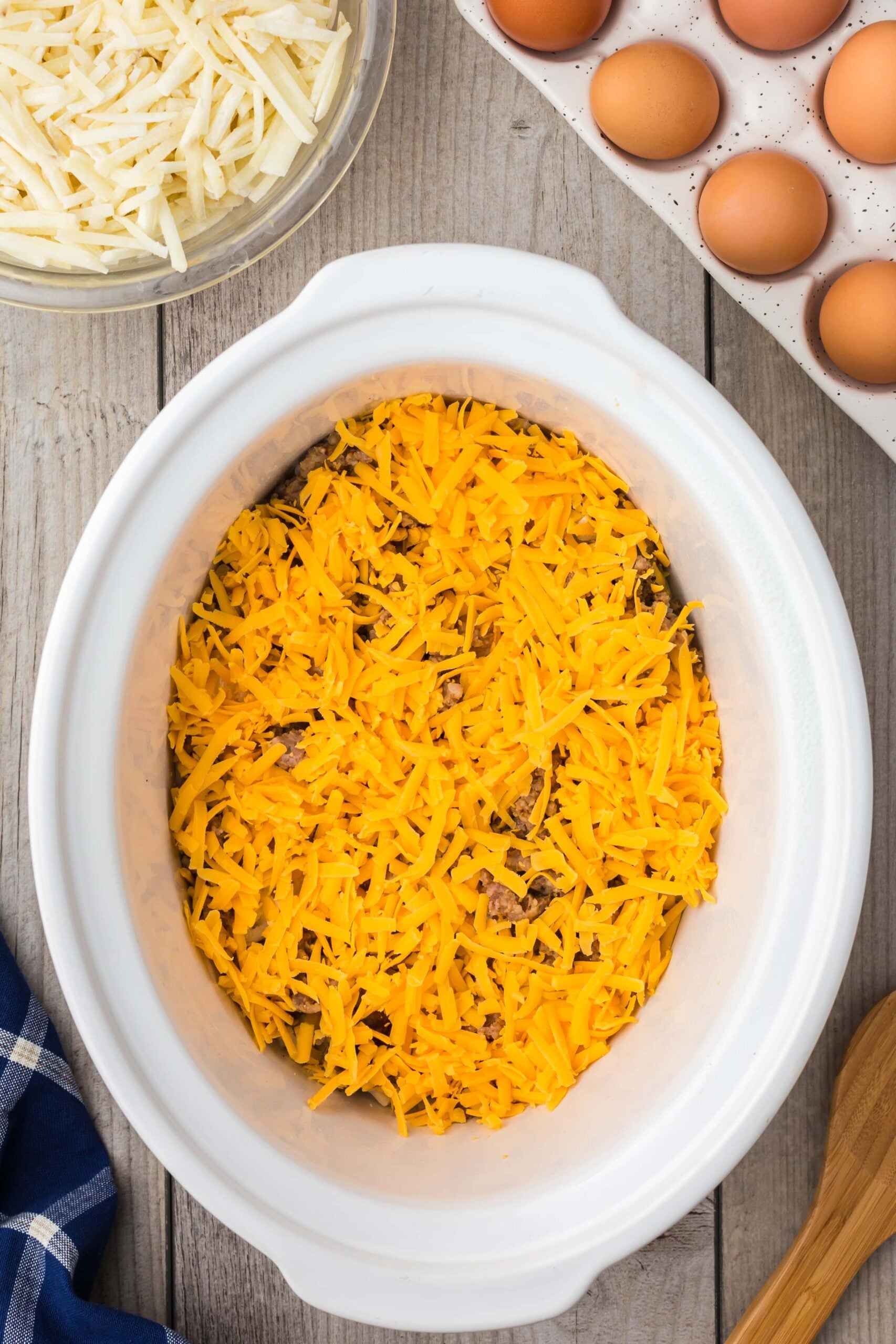 cheese, sausage, and hashbrowns layered in a crock pot for slow cooker breakfast casserole
