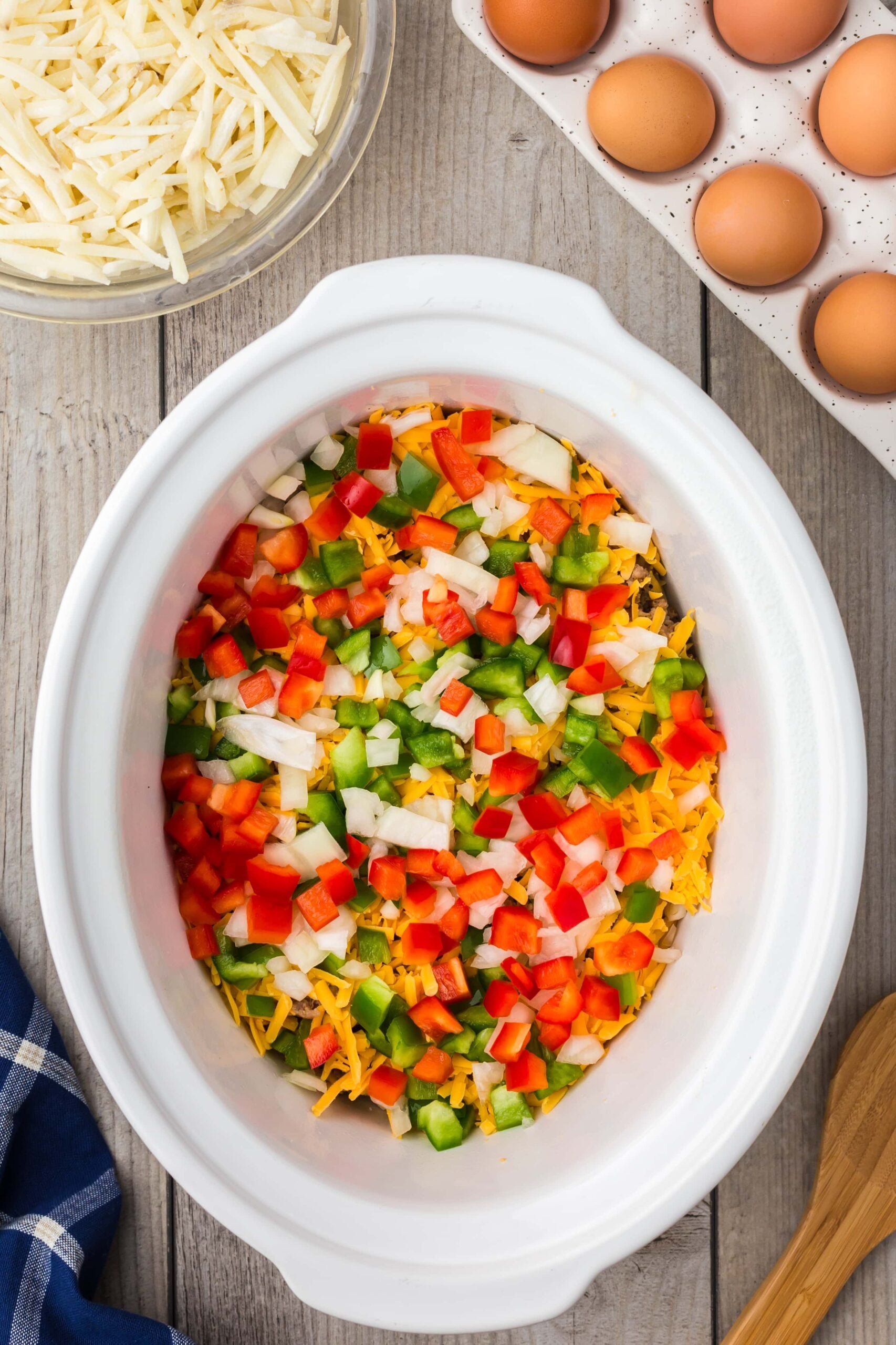 peppers/onions, cheese, hash browns, and sausage layered in a crock pot for crockpot egg casserole