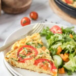A slice of vegetable frittata on a white plate with a salad on the side