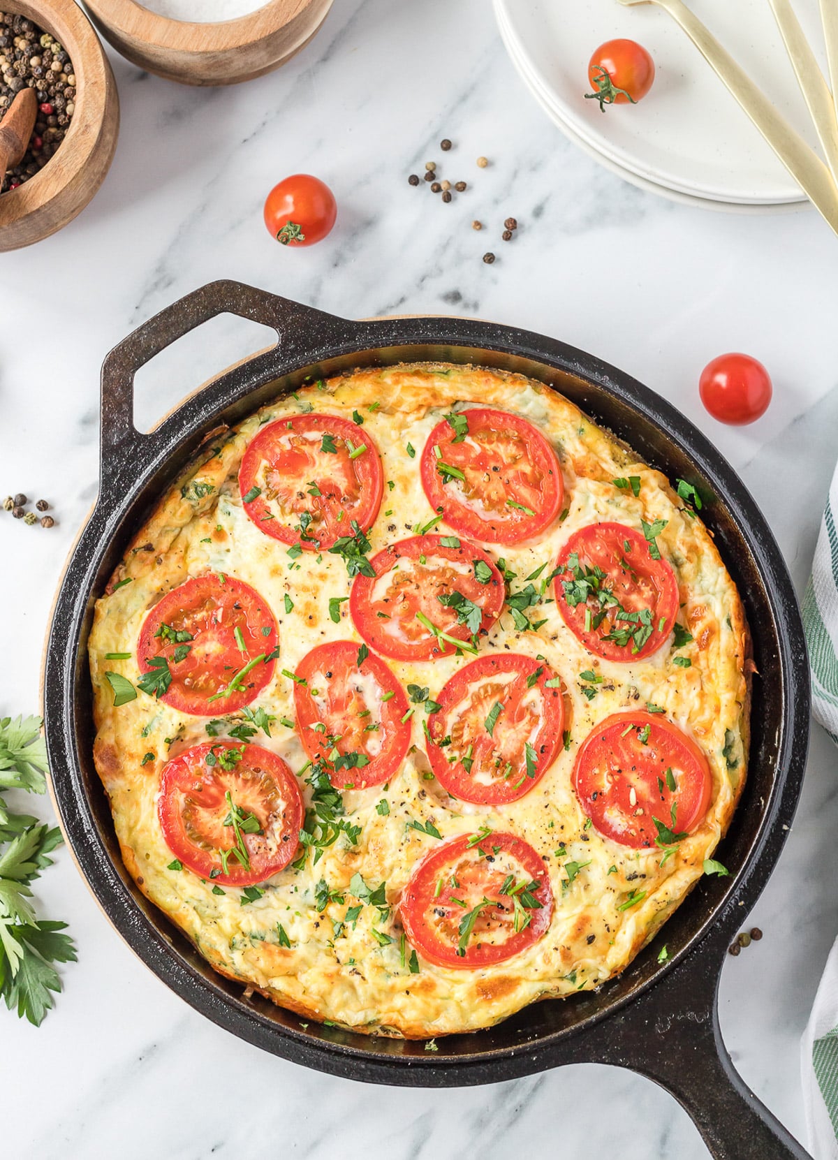 vegetable frittata in a cast iron skillet with melted cheese and cooked tomatoes on top