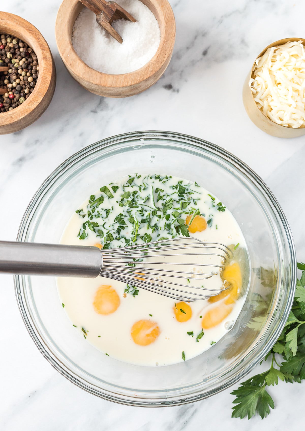 Eggs, milk and spices in a clear bowl before being mixed for a vegetable frittata