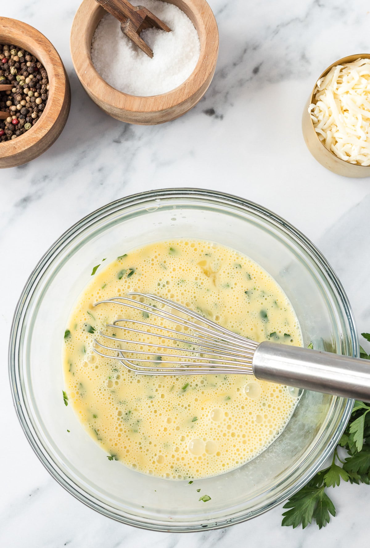 Eggs, milk and spices in a clear bowl after being mixed for a vegetable frittata