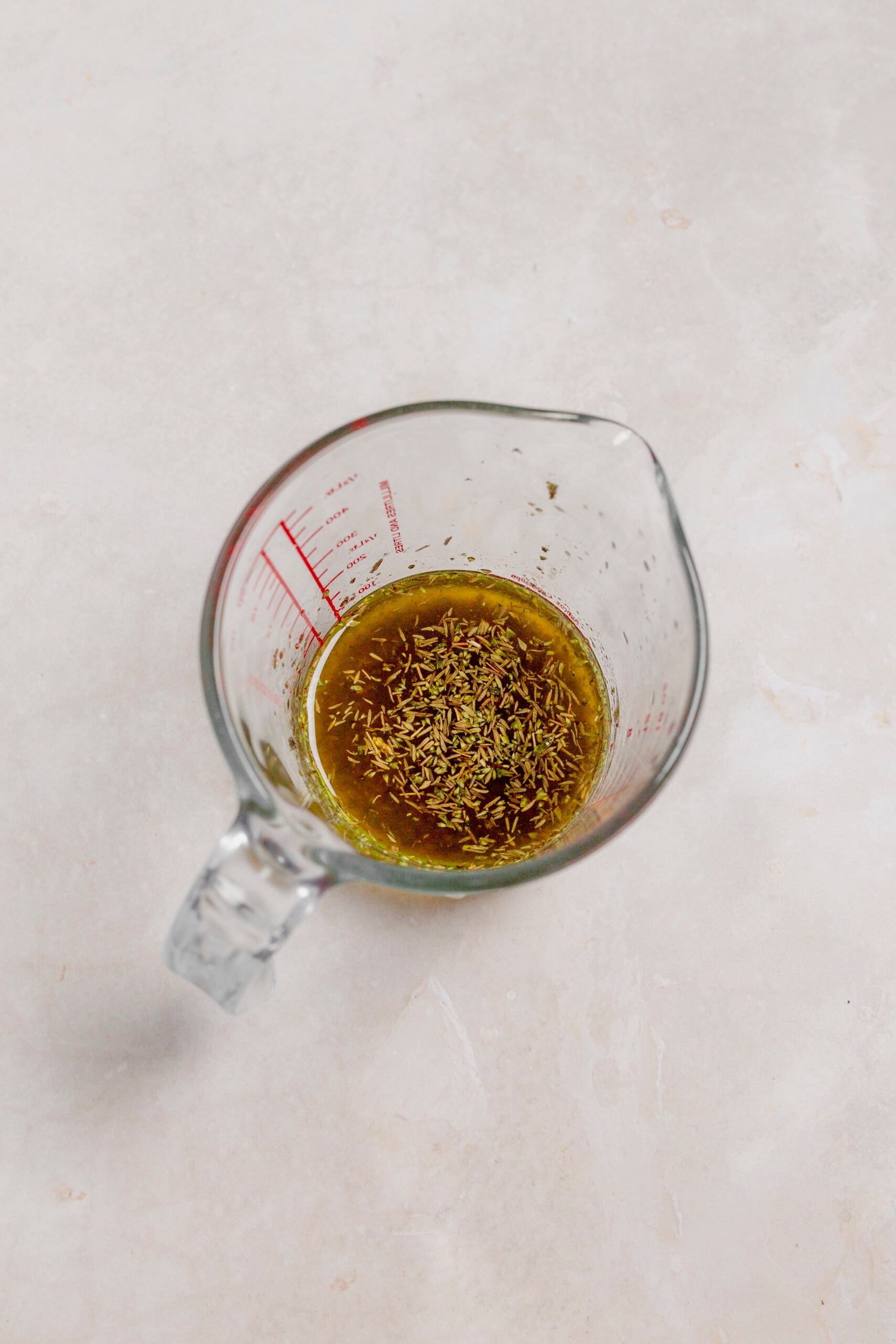 Oil, vinegar, and dried Italian spices in a measuring cup, viewed from overhead.
