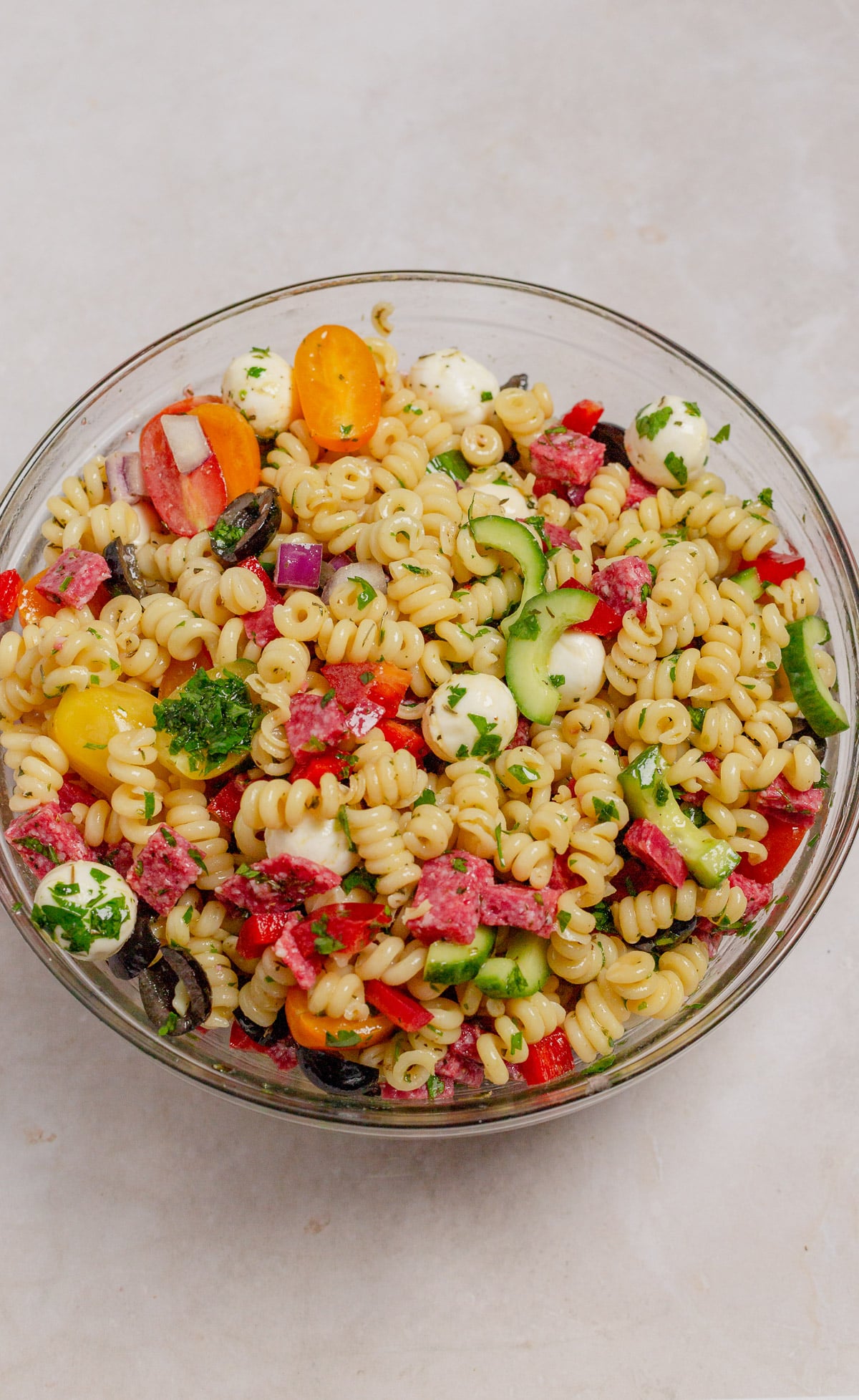 A freshly tossed pasta salad served in a glass bowl, viewed from overhead.