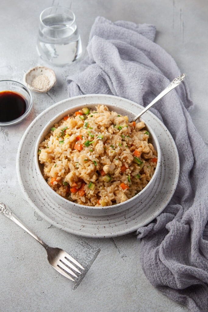 A bowl of instant pot fried rice with a fork in it and bowls of soy sauce and sesame seeds on the side