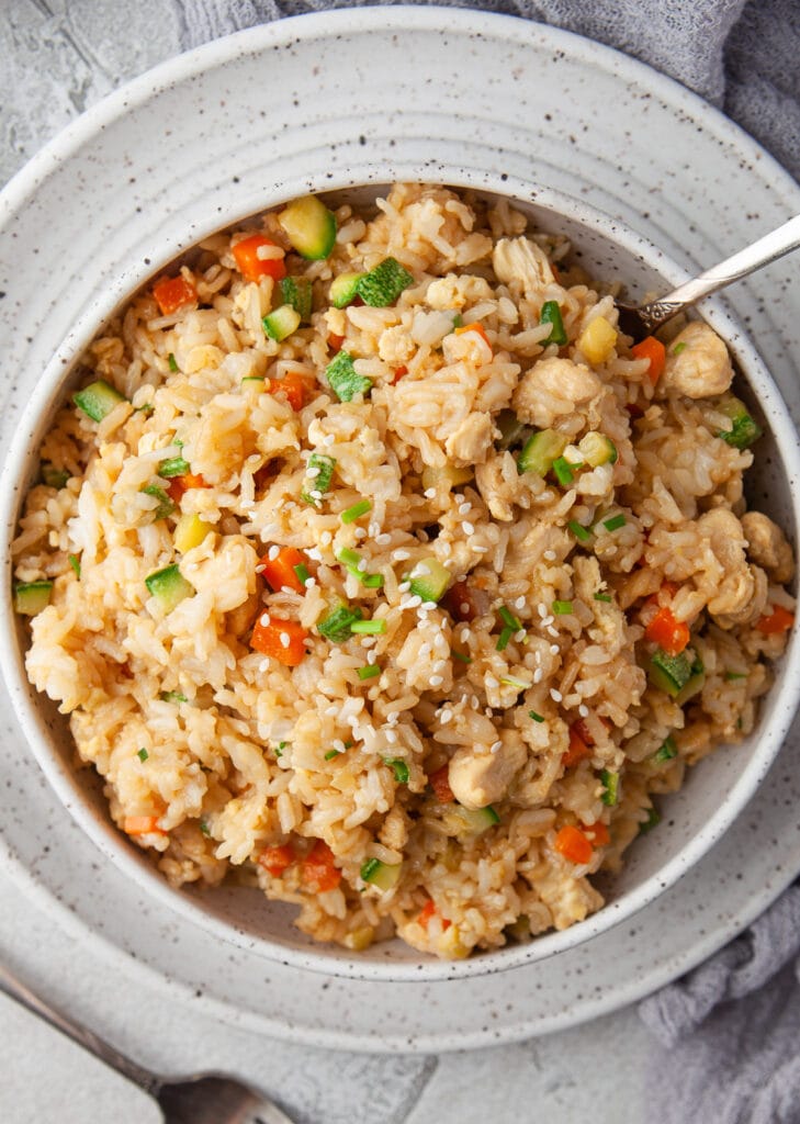 An close up shot of a bowl of instant pot chicken fried rice with a fork in the bowl