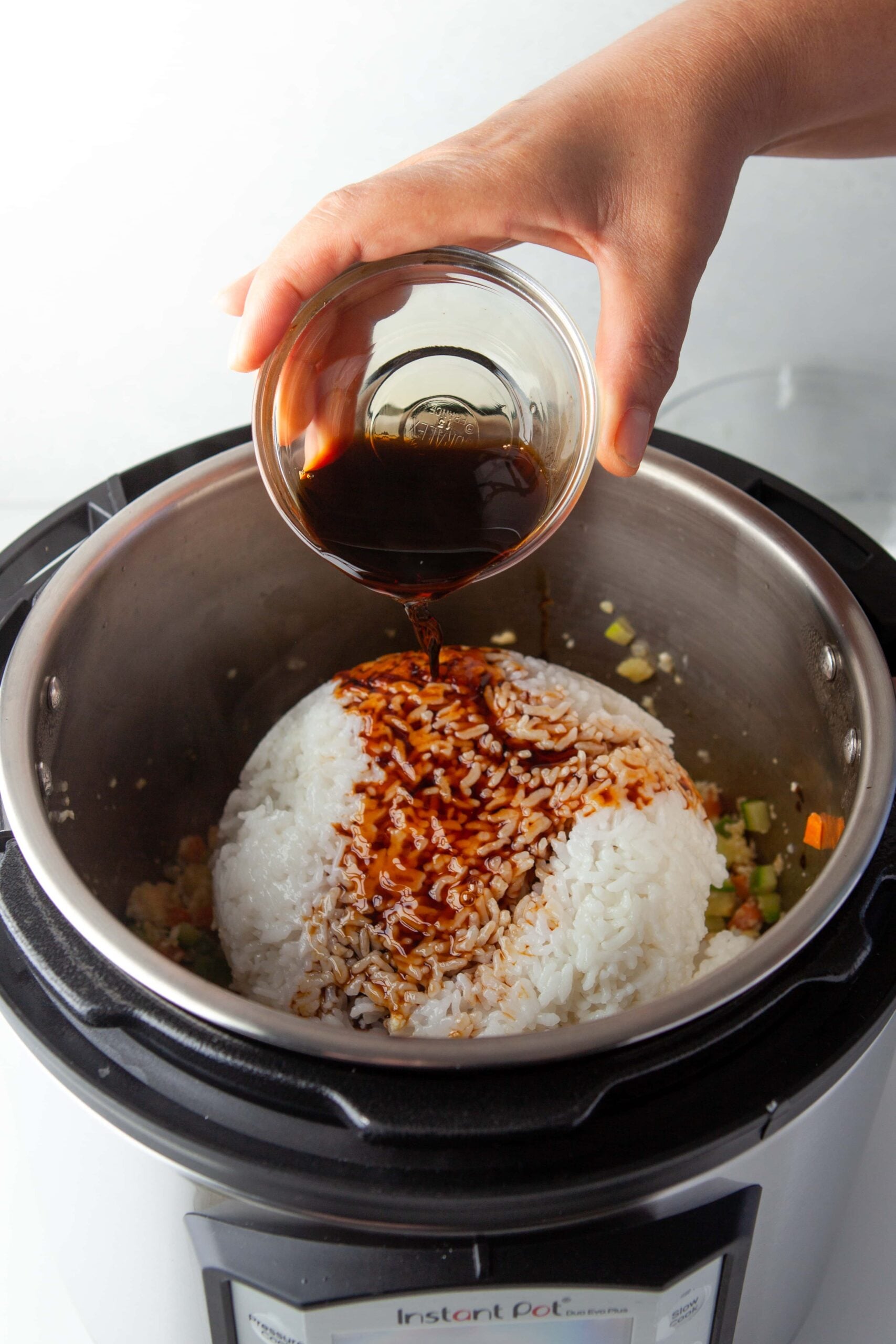 veggies and chicken in instant pot with white rice on top with soy sauce being poured on top for instant pot fried rice