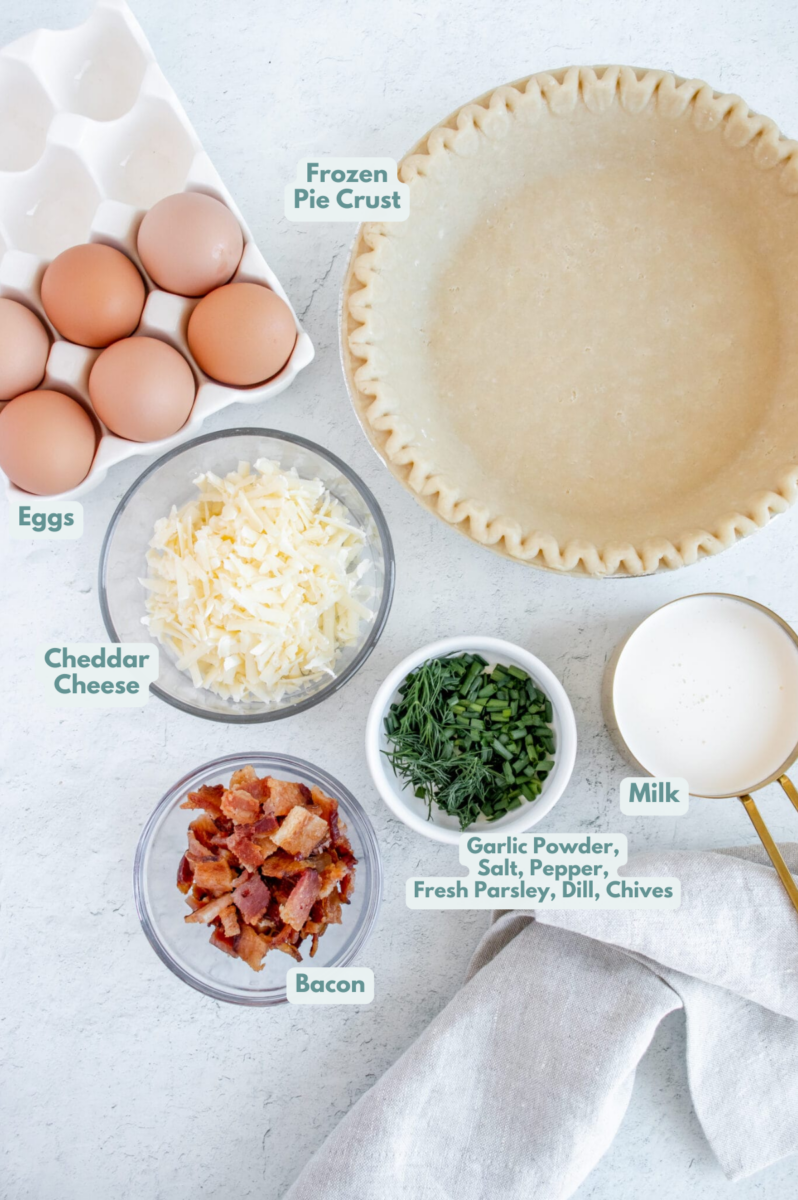 ingredients for bacon cheese quiche in clear and white bowls: pie crust, eggs, milk, bacon, white cheddar, fresh herbs