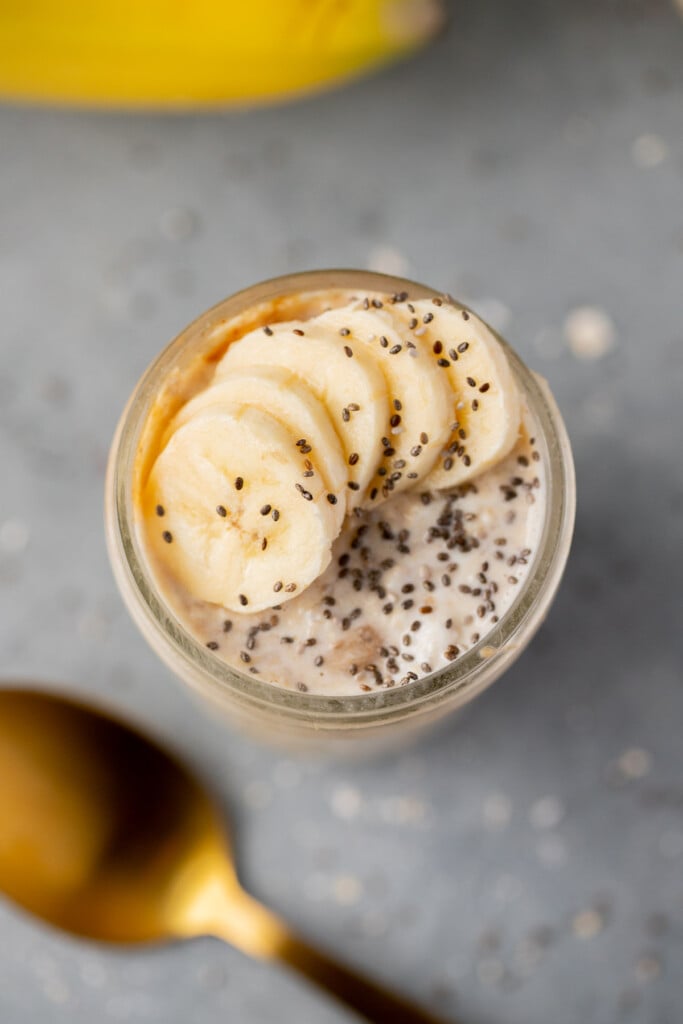 An overhead shot of a mason jar of banana overnight oats with chia seeds and sliced bananas on top