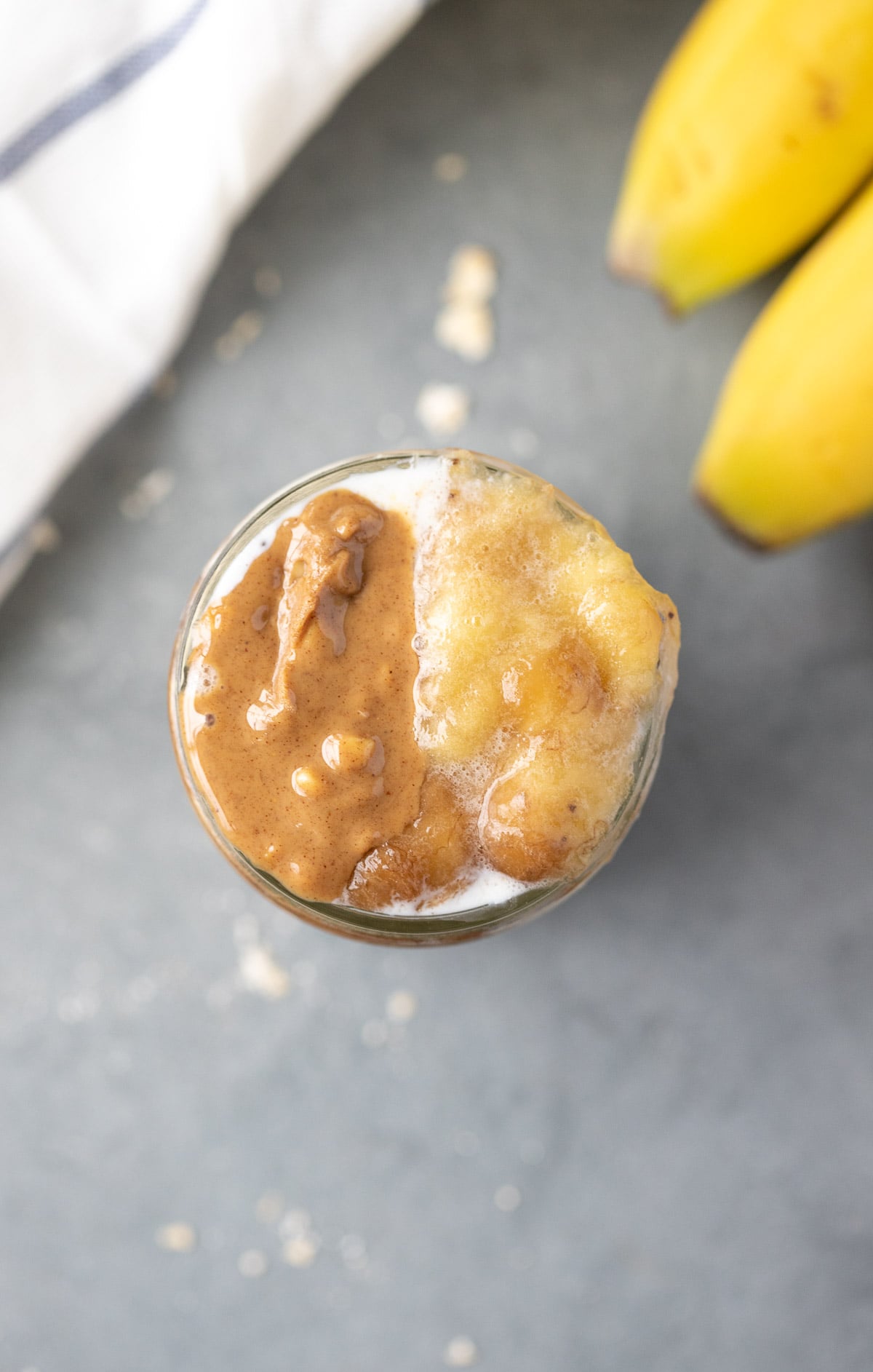 banana overnight oats in a mason jar with mashed bananas on top on a grey background with bananas in the background
