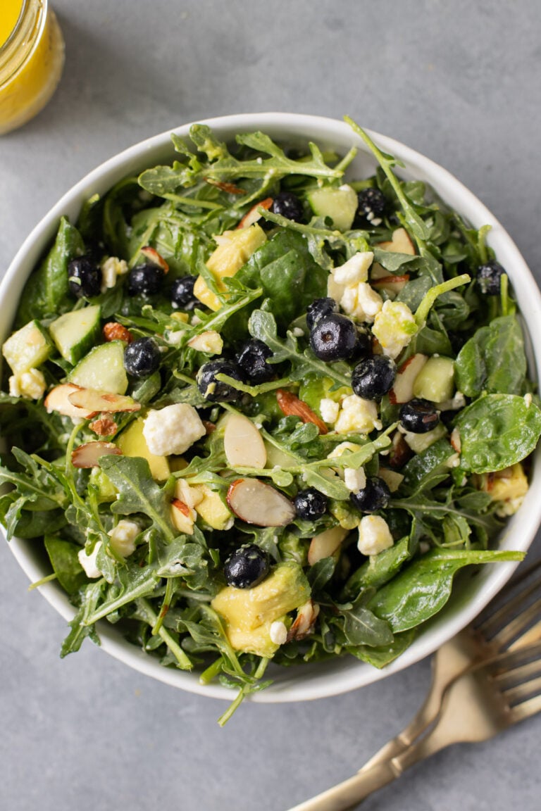 A close up of blueberry feta salad in a white bowl on a grey background