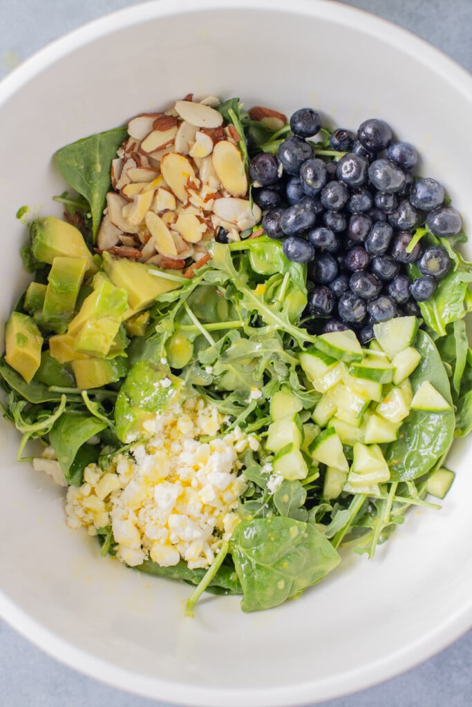 spinach blueberry salad in a white bowl segmented out in a large white bowl