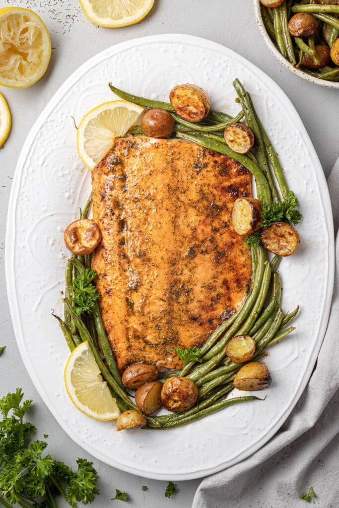 lemon salmon on a white dish with potatoes and vegetables around it