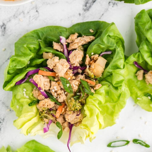 An overhead shot of a chicken lettuce wrap on a marble background with more on the side