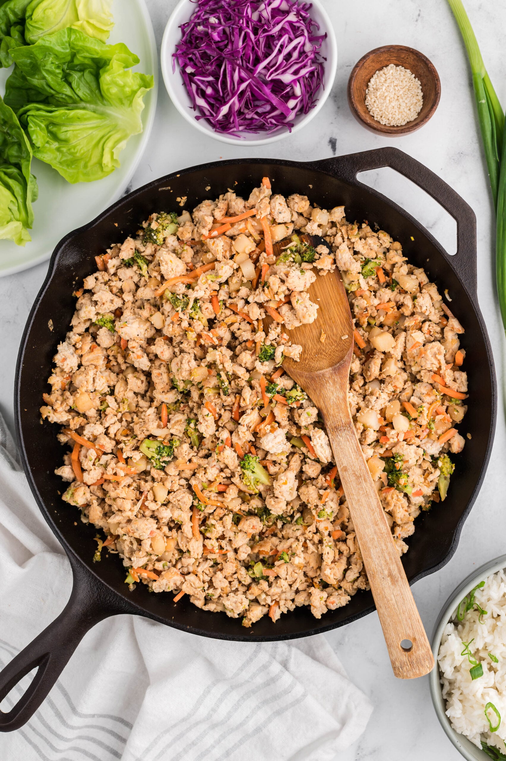 a pan of chicken mixture for healthy chicken lettuce wraps with a wooden spoon in it