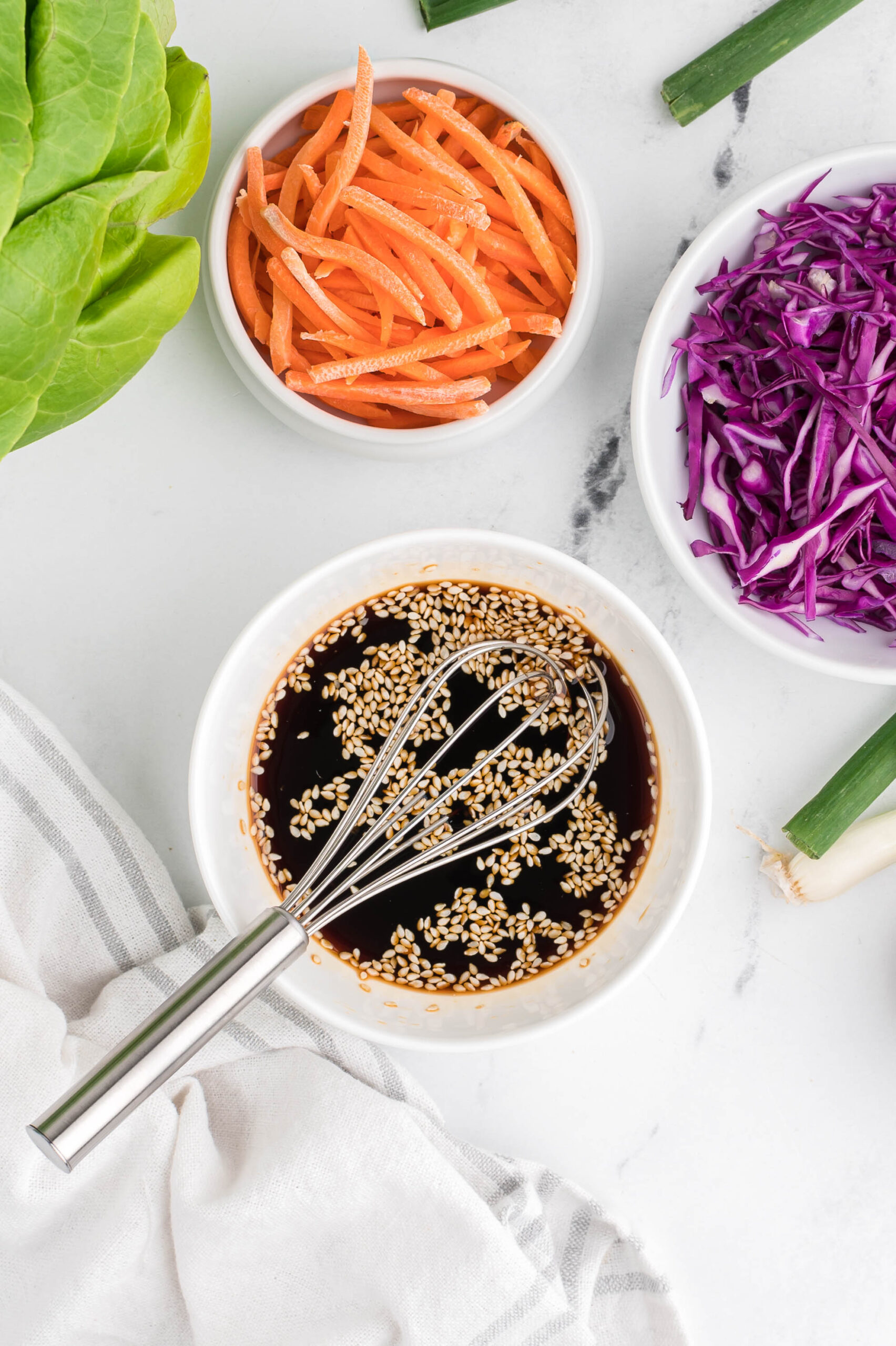 a bowl of dipping sauce with a whisk in it on a marble background with veggies on the side