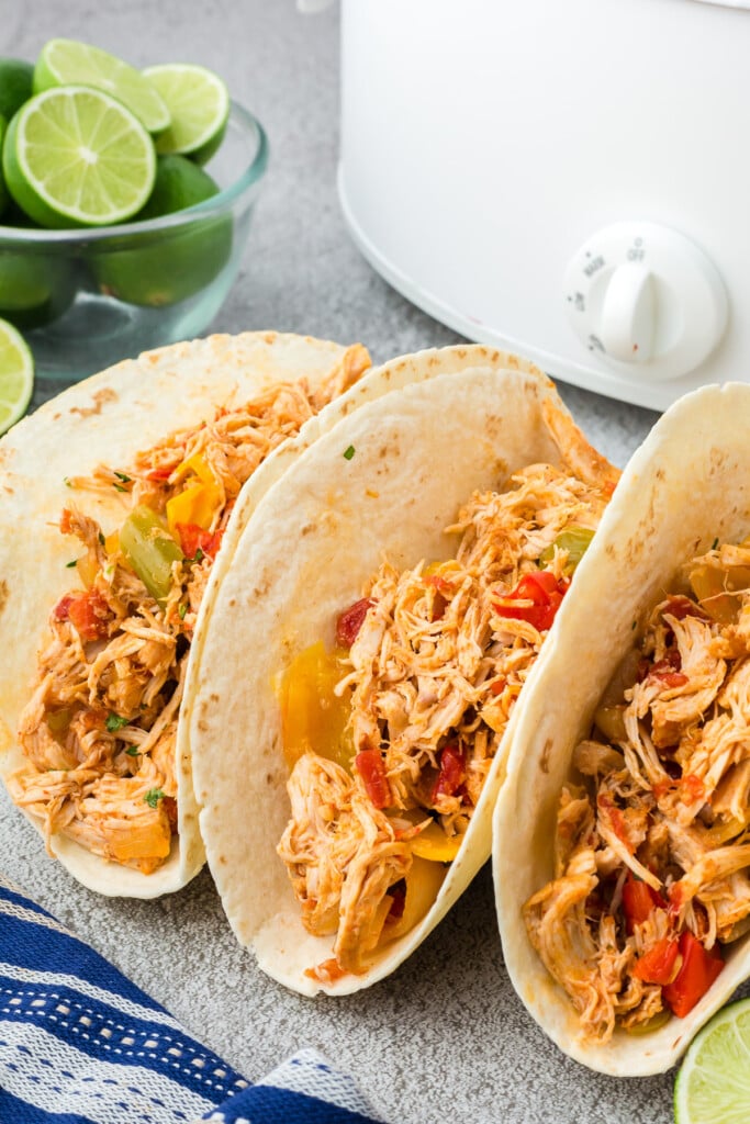 Three tortillas filled with crockpot chicken fajitas on a grey background