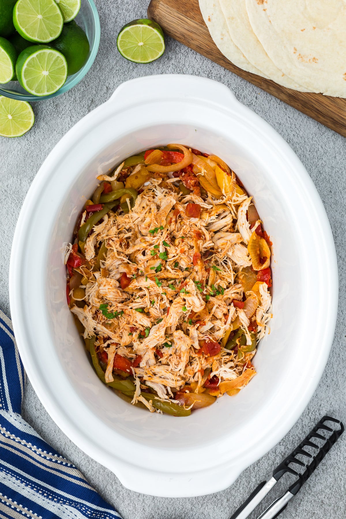 crockpot chicken fajitas in a white crockpot after being cooked and shredded on a grey background