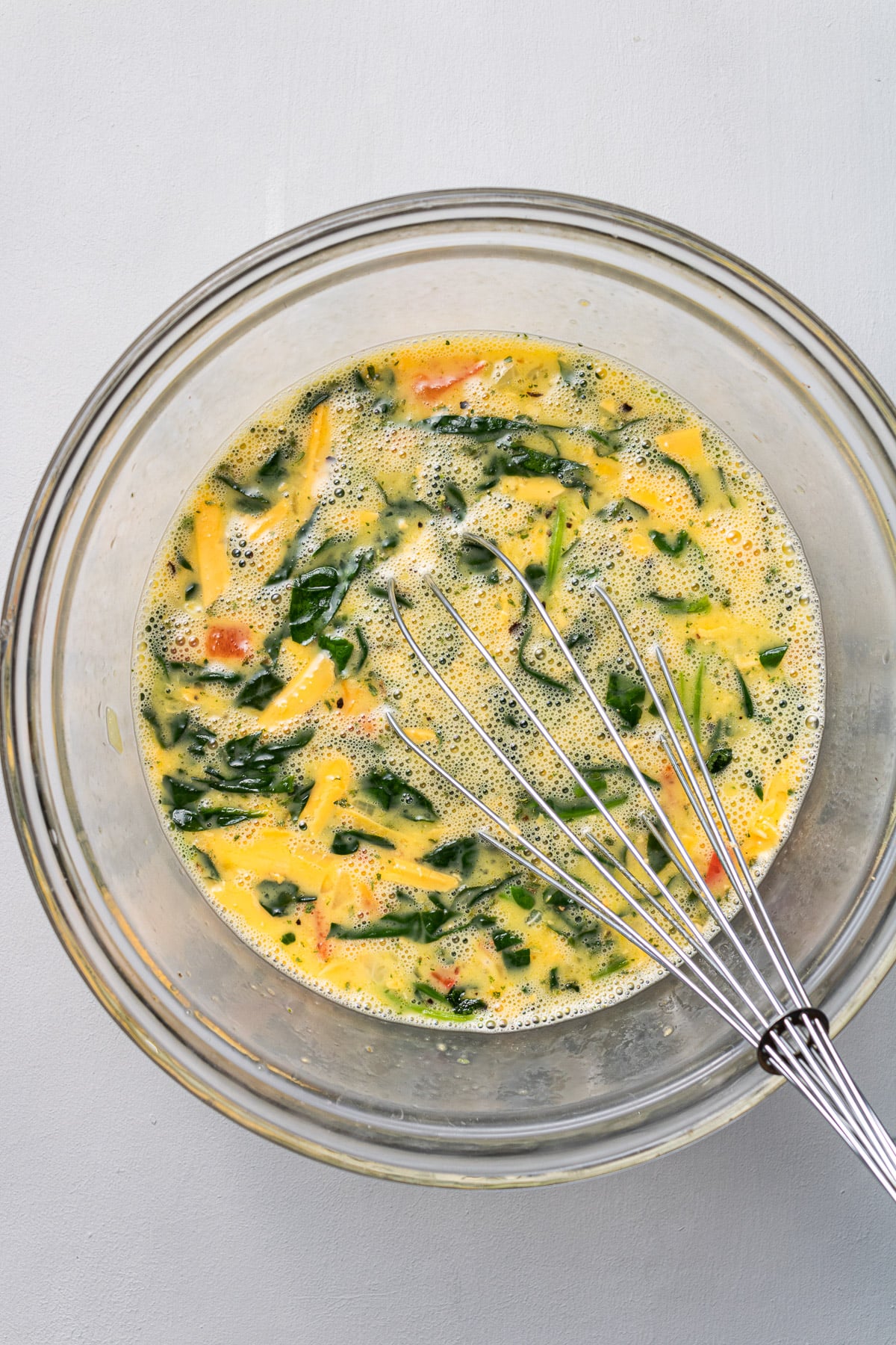 Mixture for spinach egg muffin cups being whisked together in a clear bowl