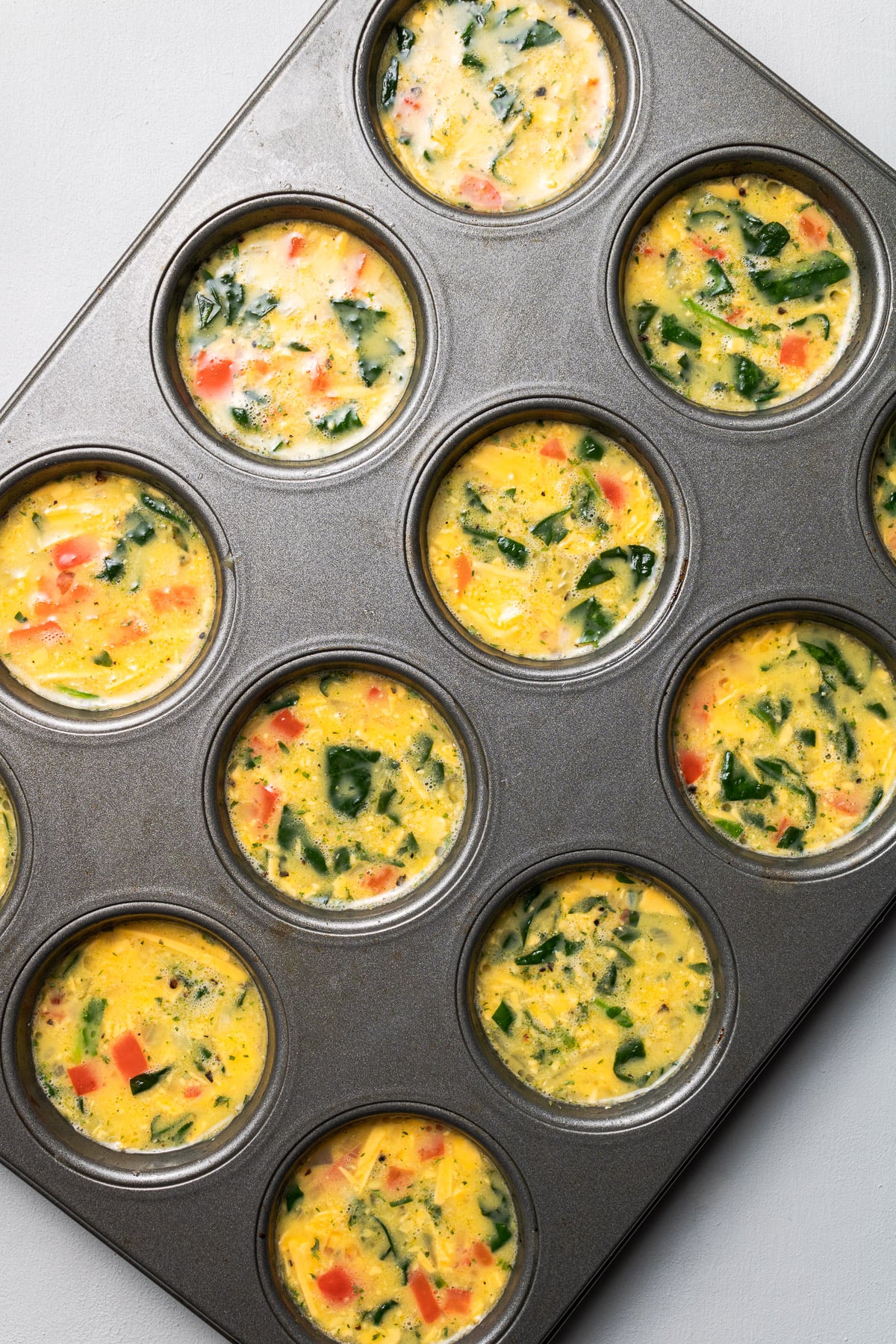 A muffin tin filled with uncooked spinach egg muffins cups