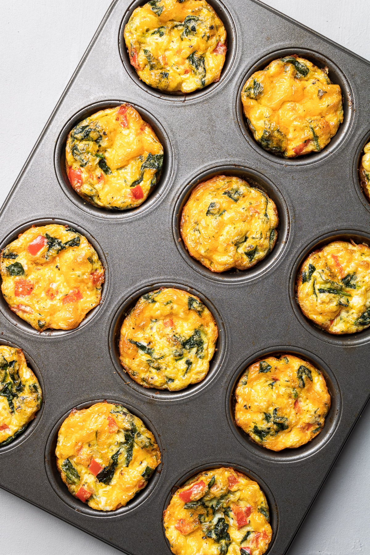 A muffin tin filled with 12 cooked spinach egg muffins cups