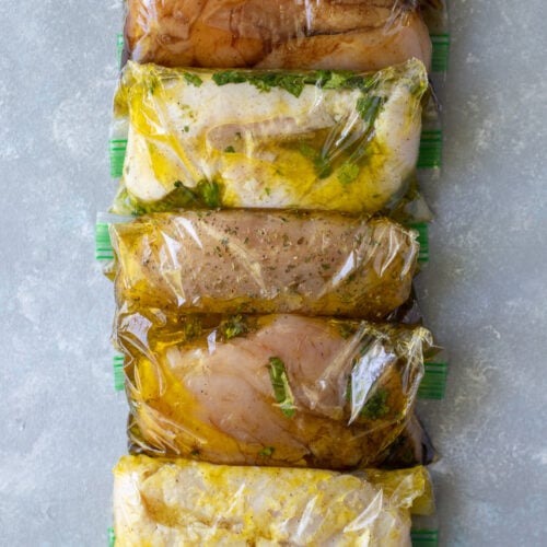 5 Healthy Chicken Marinades in individual ziploc bags on a grey background
