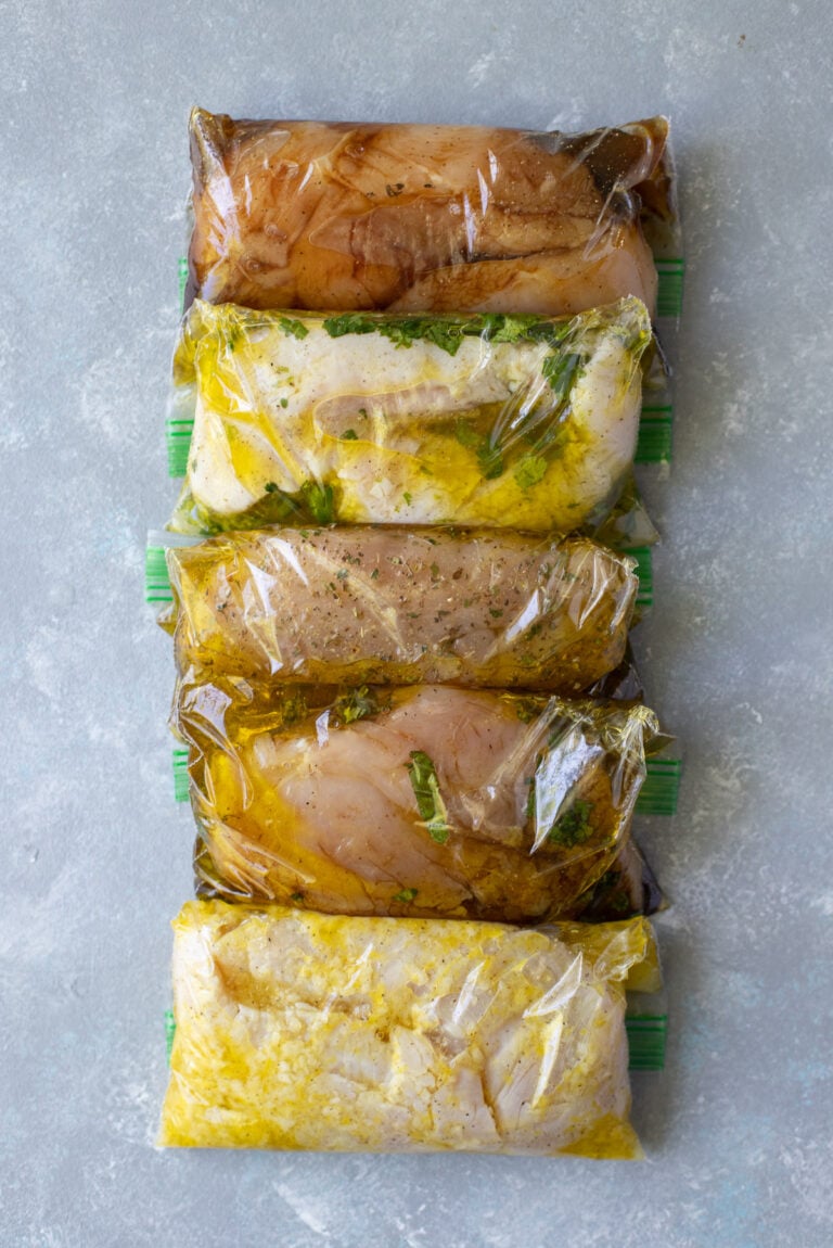 5 Healthy Chicken Marinades in individual ziploc bags on a grey background