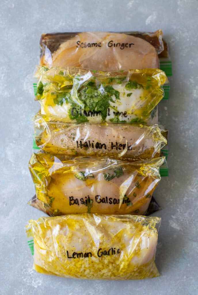 5 Healthy Chicken Marinades in ziploc bags on a grey background.